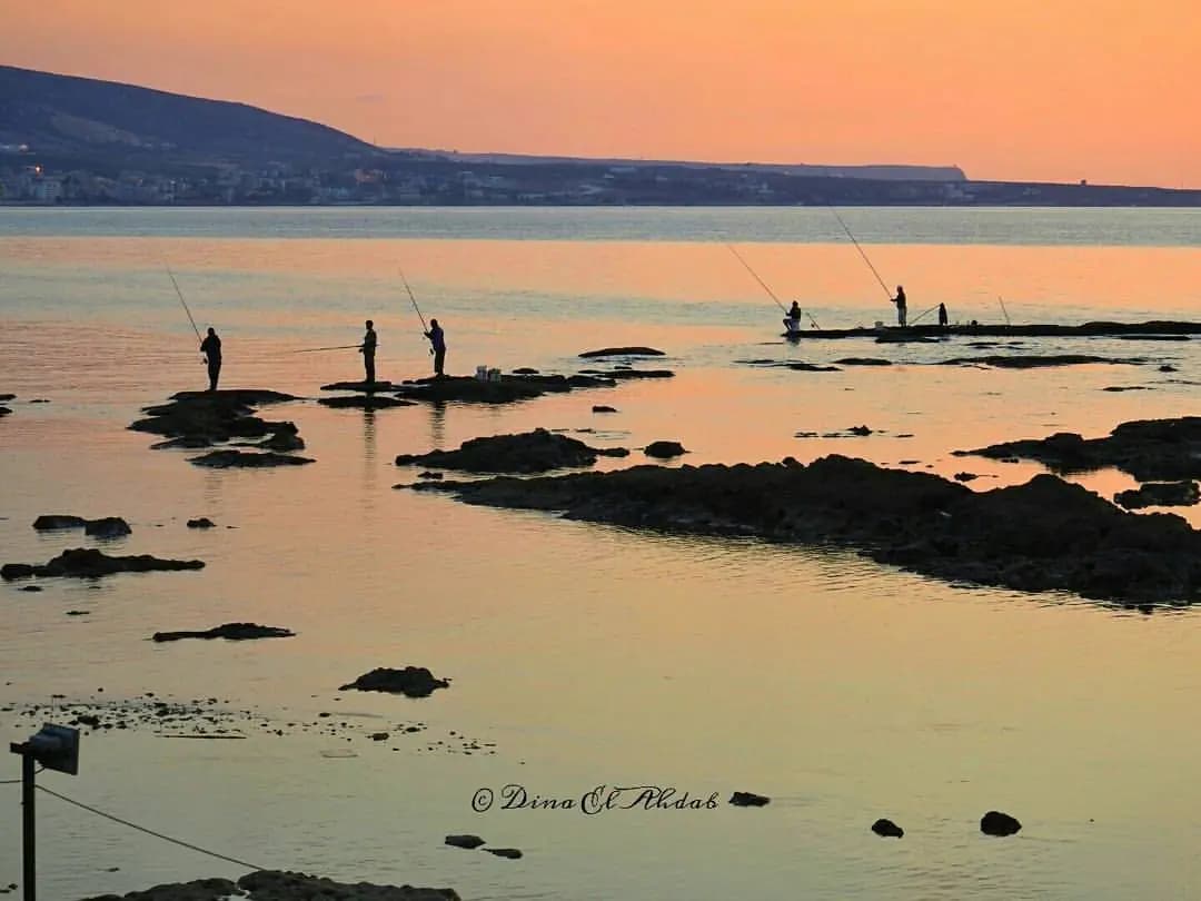 Fishermen beside El Mina's rocky coast at sunset